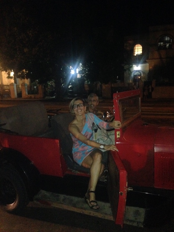 People in a red vintage convertible at night in Havana